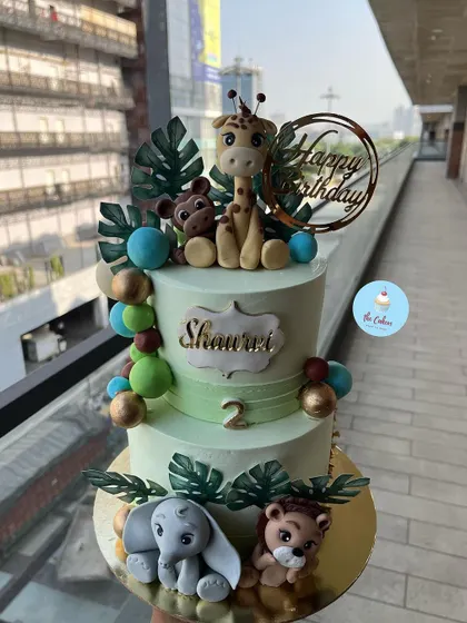 A two-tier jungle animal cake, featuring a giraffe, monkey, elephant, and lion, perfect for a child's second birthday party.