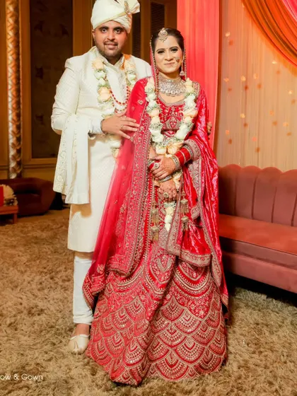 A full-length portrait of the bride and groom on their wedding day. This shot showcases the stunning detail of the bride's red lehenga and the couple's elegant presence.
