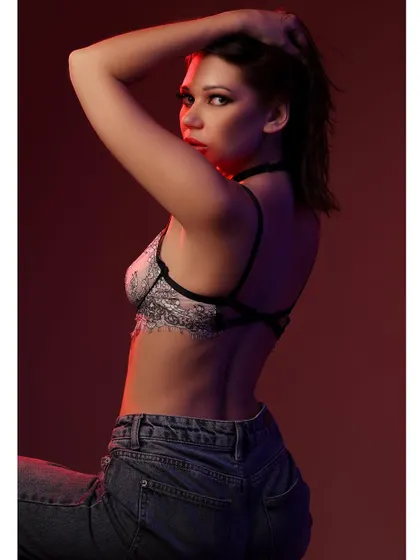 A moody portrait featuring a model in a lace bralette and denim. The red and blue lighting creates a dramatic, cinematic feel, highlighting her pose and expression.
