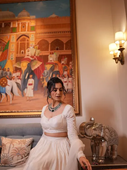 Posing in a luxurious room, this shot shows how the white lehenga complements a rich, artistic background.