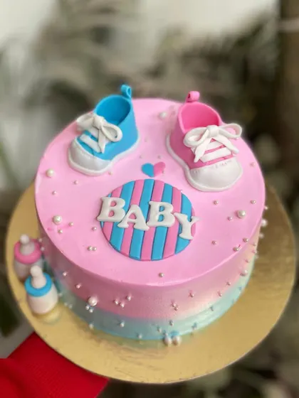 A top-down view of the baby shower cake, showing the cute fondant baby shoes and striped "BABY" plaque.