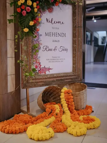 A rustic wooden welcome sign for Rinu and Tariq's Mehendi, adorned with fresh flowers and spilling marigold garlands.