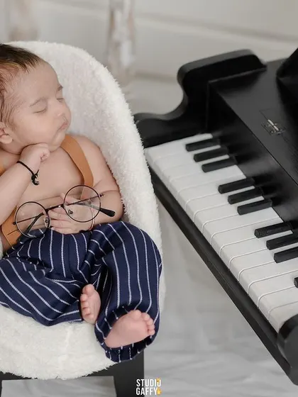 A sleepy little scholar, this newborn is posed with a pair of glasses while dozing next to the piano.