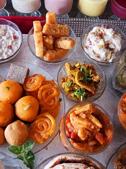 An assortment of sweets and savouries from the Janmashtami spread, including gurpara, anjeer barfi, and crispy chakli.