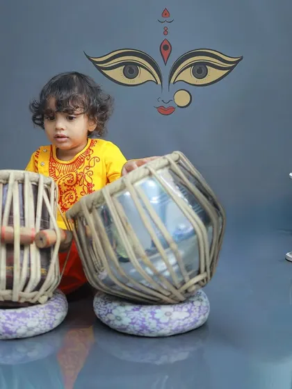 A unique and artistic portrait of a little boy with a tabla. The backdrop featuring the eyes of the Goddess Durga adds a layer of cultural and spiritual significance to this musical-themed shoot.