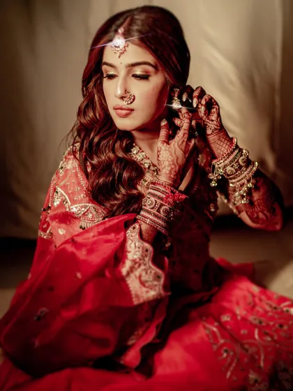 The bride adjusts her earring in a quiet, reflective moment. The soft lighting enhances the romantic feel of this look, with her wavy hair and glowing makeup.