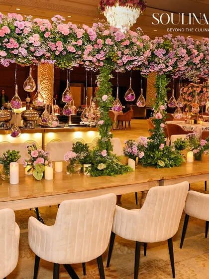 A stunning wedding dining setup featuring tables laden with lush pink floral arrangements and hanging glass ornaments. We craft immersive environments that blend romance and opulence.