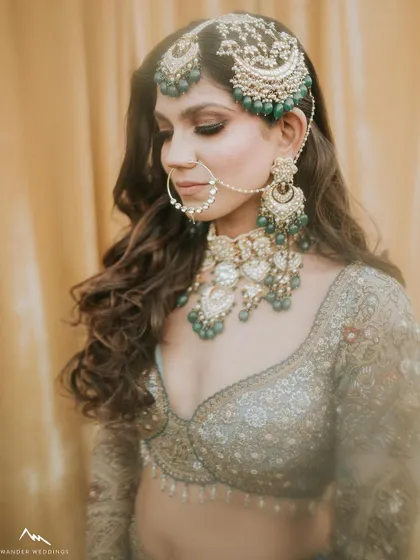 A detailed shot of the bride's profile, focusing on her intricate jewelry and the soft, smokey eye makeup that complements the green stones.