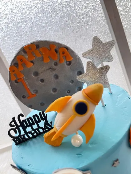 A close-up of the fondant rocket and moon topper from the space-themed cake. The name and age are personalized right on the moon.
