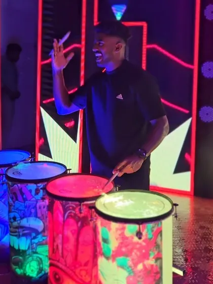 A drummer smiles as he plays the custom-painted liquid drums, with his name "ASLUICIDE" displayed on the LED screen behind him.