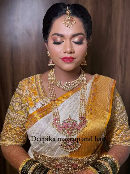 A stunning bridal look featuring a white and gold saree, bold red lips, and intricate temple jewelry.