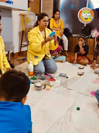 A professor guides a group of campers through a crafting activity, demonstrating the steps to create their own science-based toy.