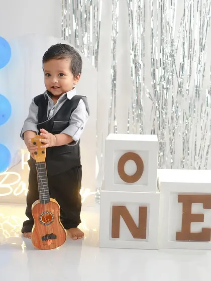 This little gentleman is ready to celebrate turning one. The simple setup with blue and white balloons and a ukulele prop allows his adorable personality to be the star of the show.