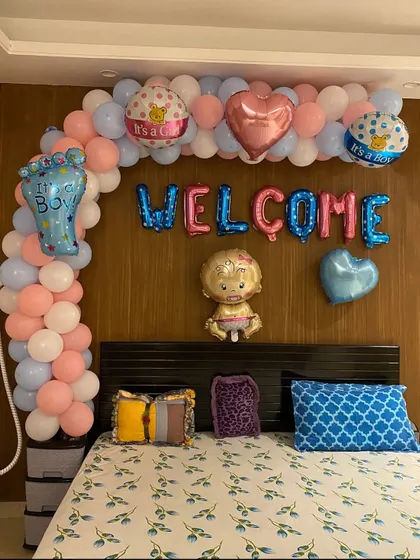 A 'Welcome Baby' decoration over a bed, using pastel pink, blue, and white balloons. The setup includes various baby-themed foil balloons.