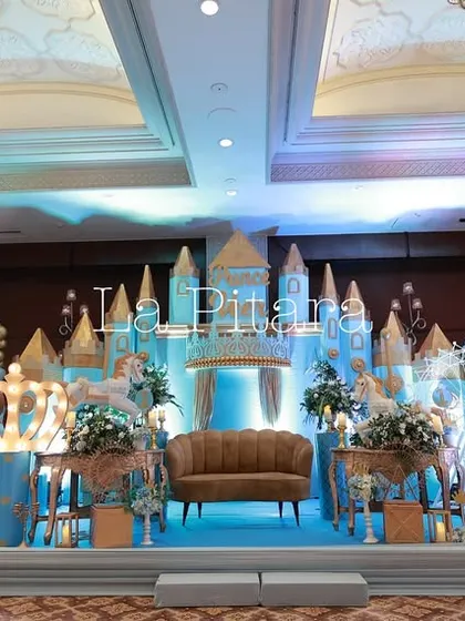 A full view of the elaborate prince-themed stage, illuminated with blue lights to create a magical nighttime castle effect. The setup includes multiple photo frames and large crown props.