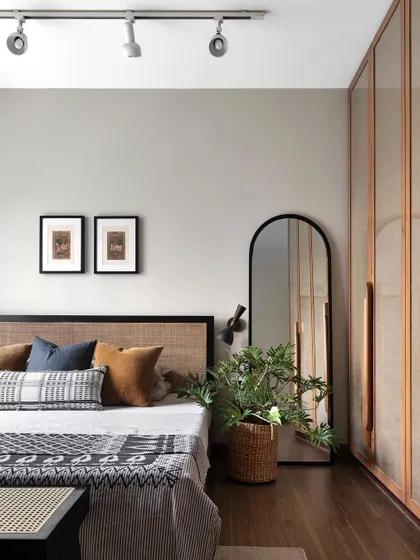 A serene bedroom in the 'Ikigai Living' apartment. The rattan bedhead, jute-paneled wardrobe, and woven textiles create a calm, nature-inspired retreat from the city.