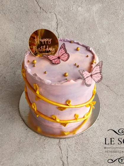 A whimsical cake with butterflies on a golden creeper. This 1 kg Lemon Coconut cake features a purple watercolor buttercream effect and delicate pink wafer paper butterflies.