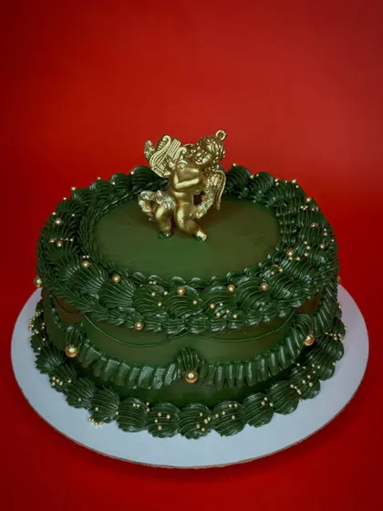 A touch of vintage elegance for the holidays. This deep green Christmas cake is decorated with classic piping, gold sprinkles, and a cherub topper for a timeless look.