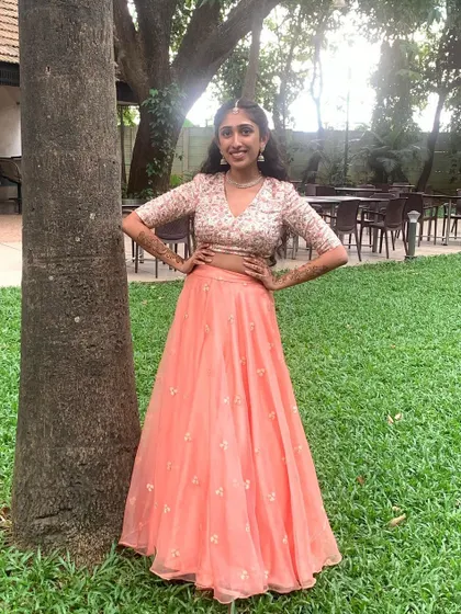 This client looks absolutely lovely in her custom crop top and skirt, perfect for a Sangeet. The embroidered blouse and flowing peach skirt create a look that is both festive and comfortable.