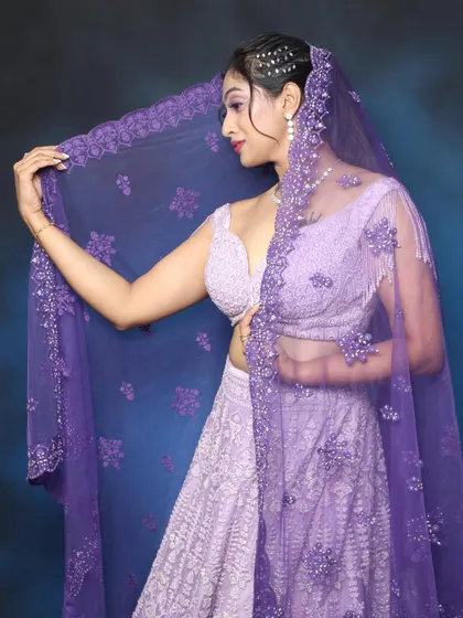 A dramatic pose with a sheer purple dupatta. The makeup is soft yet glamorous, with a focus on the beautiful lilac eyeshadow.