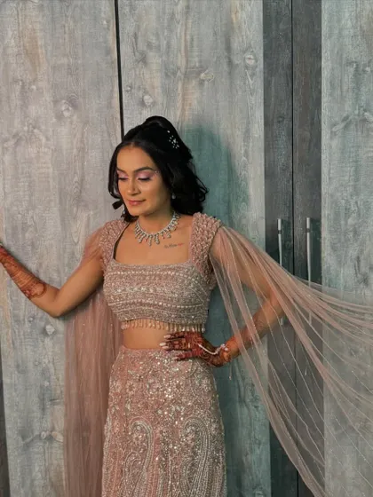 This bride is ready for her sangeet night. The shimmery pink lehenga is paired with dramatic eye makeup and a sleek high ponytail for a full glam effect.
