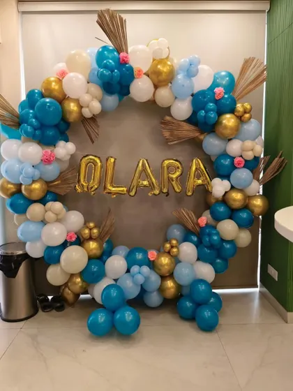 A full balloon ring in blue, white, and gold with the baby's name in foil letters. Dried palm leaves add a touch of boho chic to this welcome home decor.