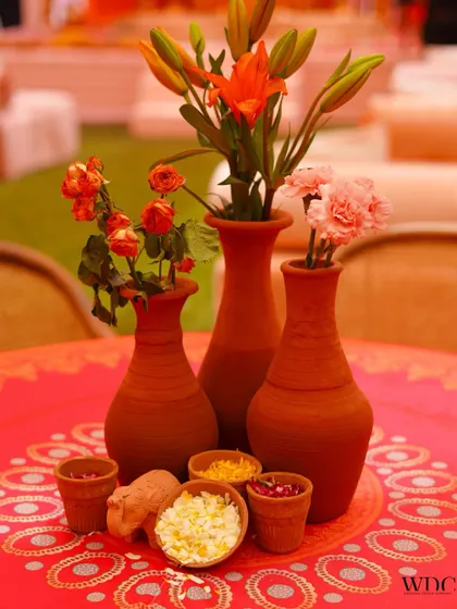 A detailed shot of a tabletop centerpiece. We used an assortment of terracotta vases with fresh flowers, alongside small clay pots filled with flower petals, to create an authentic and charming look.