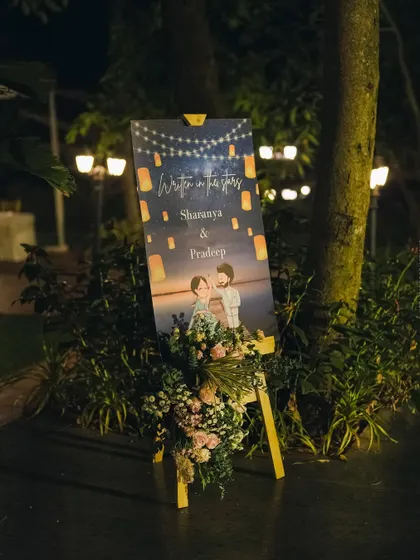 The custom welcome sign lit up at night, surrounded by lush greenery and soft lighting.