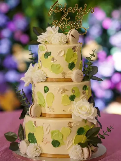 A beautiful three-tier cake in shades of green for a lovely couple's big day. The design features a modern palette-knife texture, fresh flowers, and delicate macarons.