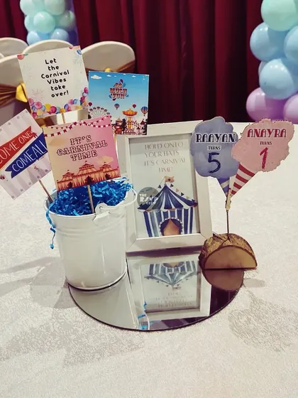 A centerpiece for a shared birthday carnival, with custom signs for both birthday kids.
