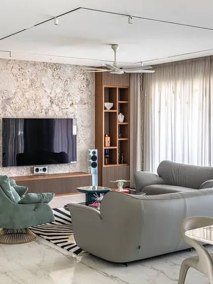The living room from the 'Urban Oasis' project, showing a mix of textures and colors. A textured TV wall is flanked by wooden shelves, while teal armchairs add a pop of color.