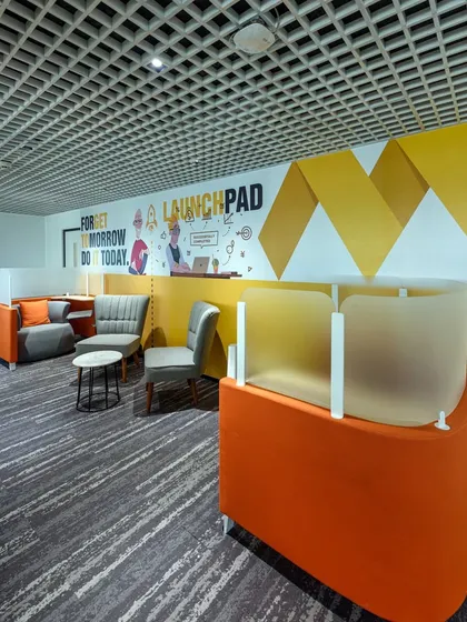 A breakout space with unique orange seating pods that offer a degree of privacy. The wall features a graphic with the motivational phrase "Forget tomorrow, do it today."