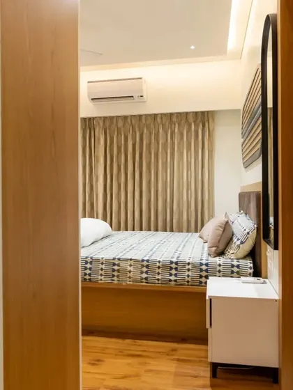 A glimpse into a cozy bedroom corner. The design features a storage bed with a veneer finish and a simple, white PU-finished bedside unit, creating a warm and inviting atmosphere.