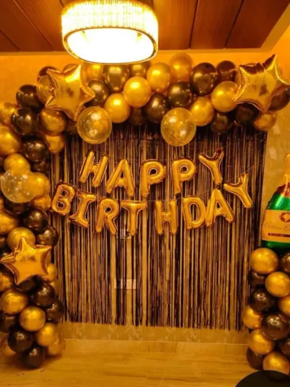 A classic and stylish birthday decoration in black and gold. This setup includes a balloon arch, a shimmering tinsel backdrop, and large "Happy Birthday" foil letters, perfect for an elegant celebration.