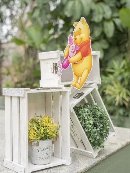 Winnie the Pooh and Piglet props set among rustic white crates. This combination of character cutouts and simple decor elements creates a charming, storybook feel.