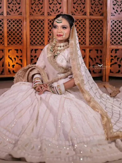 A wide shot of the bride seated gracefully in her white chikankari lehenga. The composition emphasizes the elegance and grandeur of the traditional yet modern outfit.