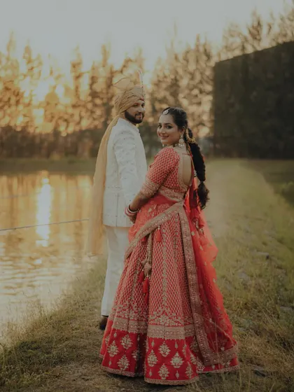 A lovely portrait from their pre-wedding shoot. The bride looks back with a smile as they walk along the water's edge at sunset.