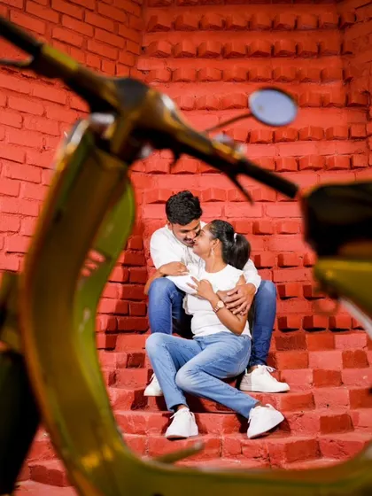 A creative shot through the handlebars of a scooter, framing the couple sharing a moment on a set of red stairs.