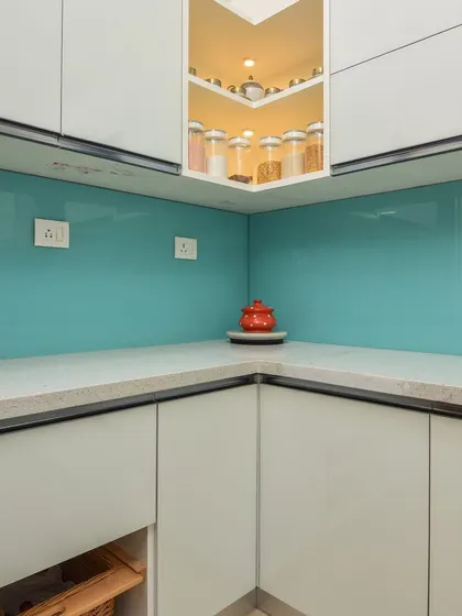 A corner detail of the kitchen, showing the illuminated open corner shelf and the seamless countertop. Every inch of space is utilized effectively.