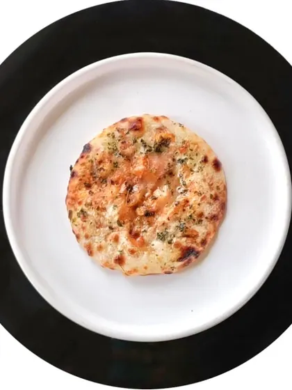 A single, perfectly round kulcha, topped with herbs and baked to perfection. It represents the simple elegance that underlies even our most inventive creations.