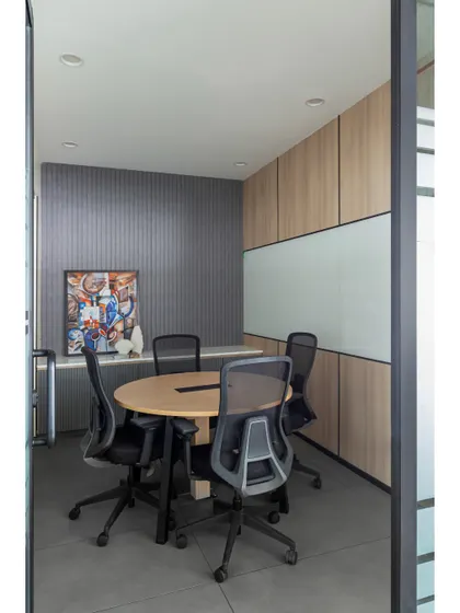 A smaller meeting room designed for team huddles. It features a round table to encourage inclusive discussion, fluted wall paneling for texture, and a vibrant piece of art to spark creativity.