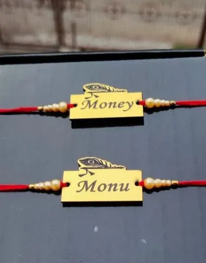 A pair of matching metal rakhis, personalized with names and a feather charm.