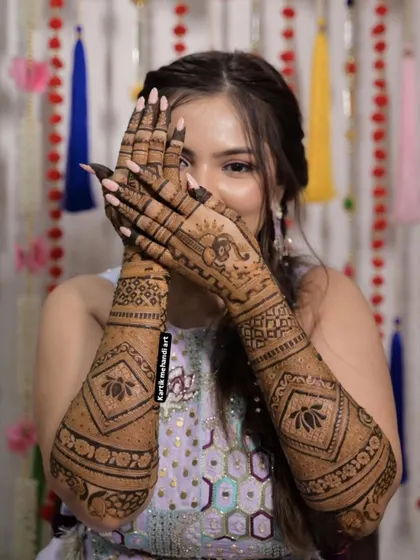 A playful pose highlighting the beautiful back-hand mehandi. The design includes lotus motifs and a Ganesha figure, blending modern and traditional elements.