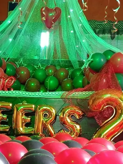 A 'Cheers to 2 years' anniversary celebration. This room is decorated with red, green, and black balloons, a canopy with green lights, and large foil balloons marking the occasion.