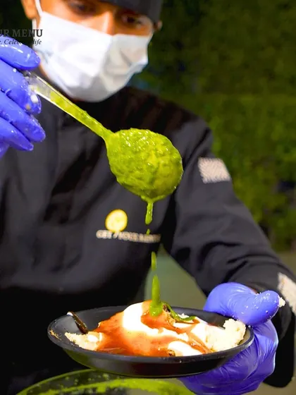 The vibrant green mint and coriander chutney being drizzled over a chaat dish. We make all our chutneys in-house using fresh ingredients for the most authentic taste.