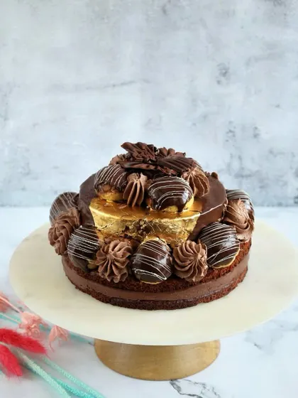 Another look at our Desire 3 Cake, standing tall on a marble platter. The combination of chocolate-dipped choux buns, gold varak, and rich mousse makes it a true work of art.