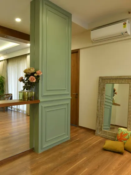 A wainscoted pillar painted in sage green acts as a beautiful partition in the master bedroom. A large, rustic-framed mirror leans against the wall, adding a touch of casual elegance.