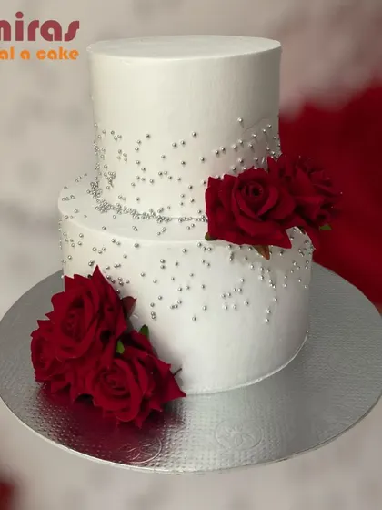 A stunning two-tier wedding or anniversary cake. The simple white design is adorned with deep red roses and sprinkled with silver pearls for a look of classic romance.