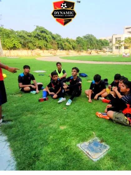 A coach sits with his team on the grass, having a tactical discussion after a practice session.