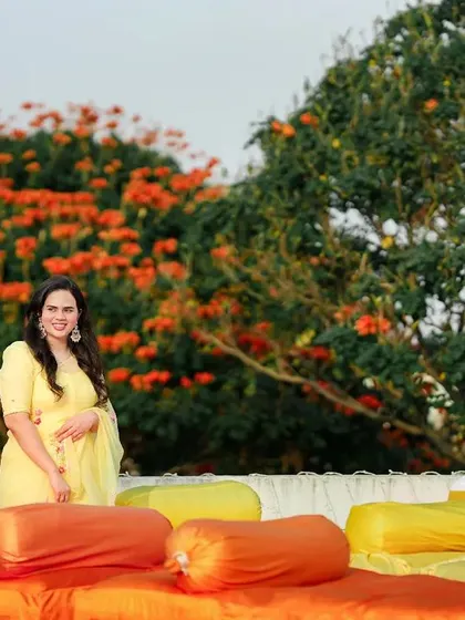The bride, glowing in a yellow outfit for her Haldi ceremony. The vibrant orange and yellow decor creates a cheerful and festive atmosphere.
